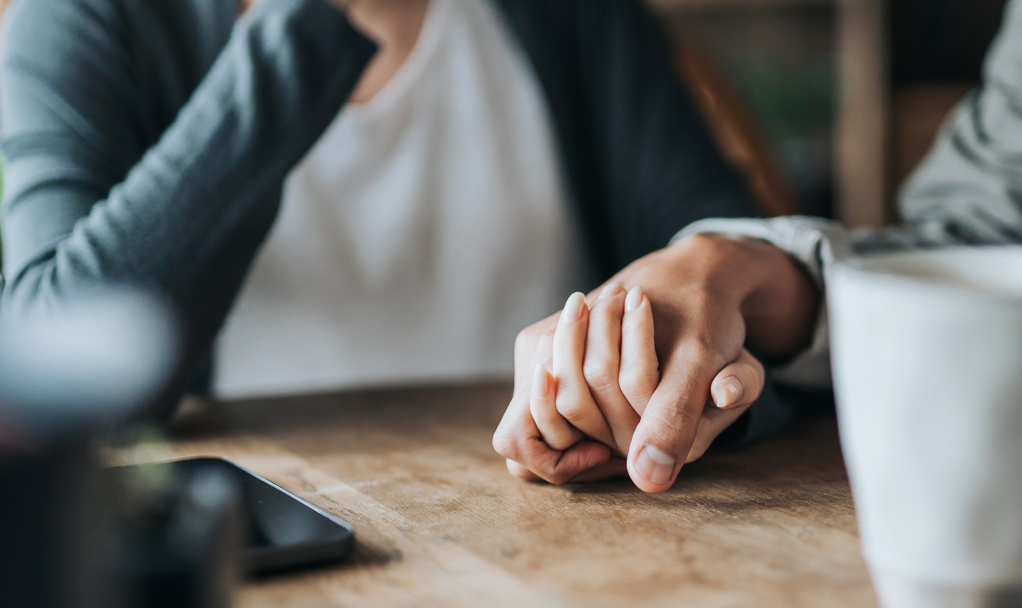 Two hands holding on a wooden table.