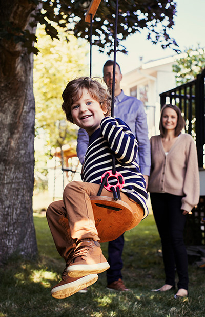 Beckett on swing smiling while his parents are watching.