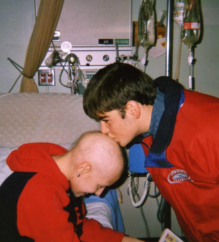 Joey and alyssa in a hospital room. Joey is kissing the top of Alyssa's head, which has lost hair due to treatment.