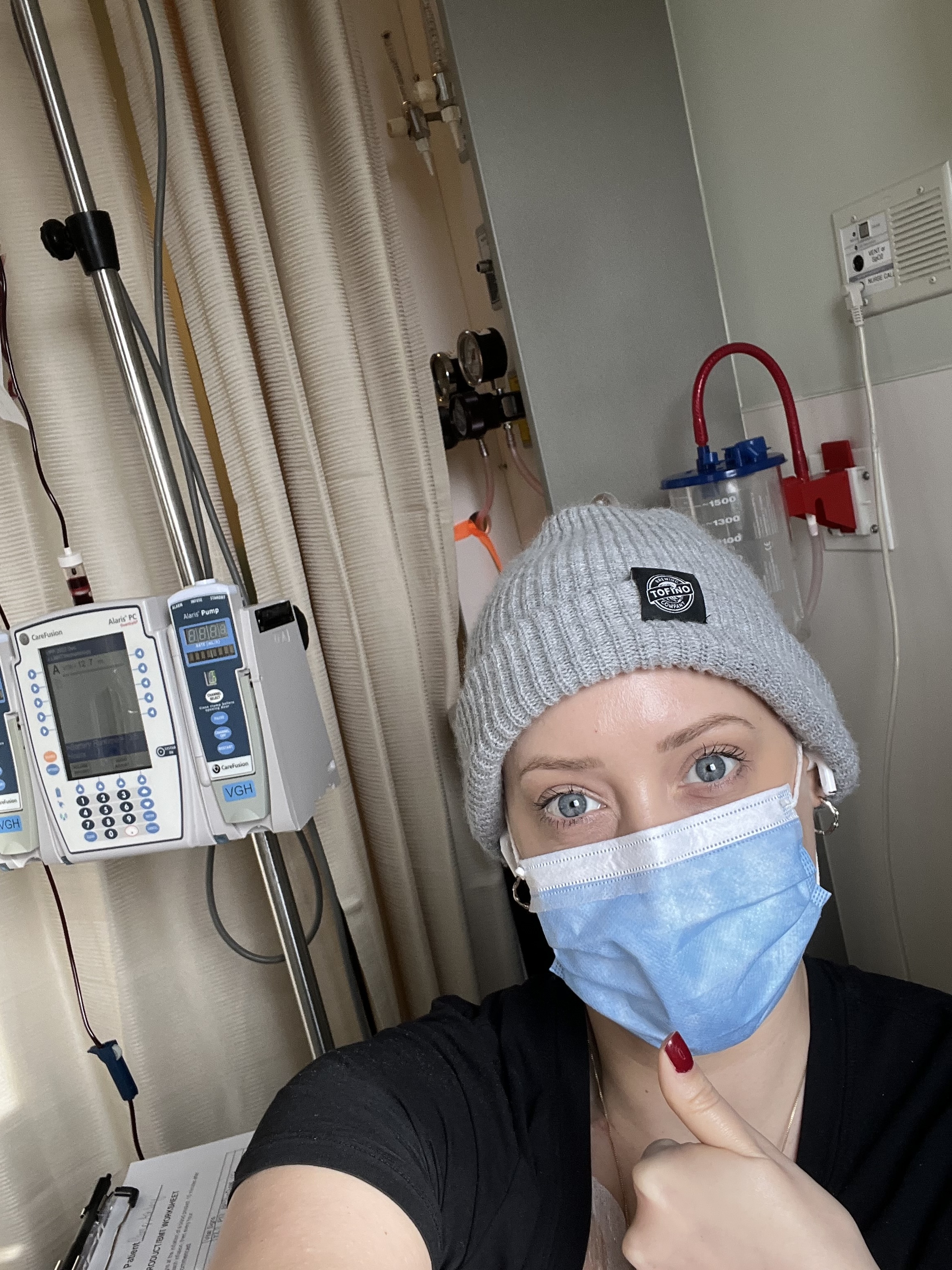 Ashley wearing a mask in a hospital room, with a thumb up.