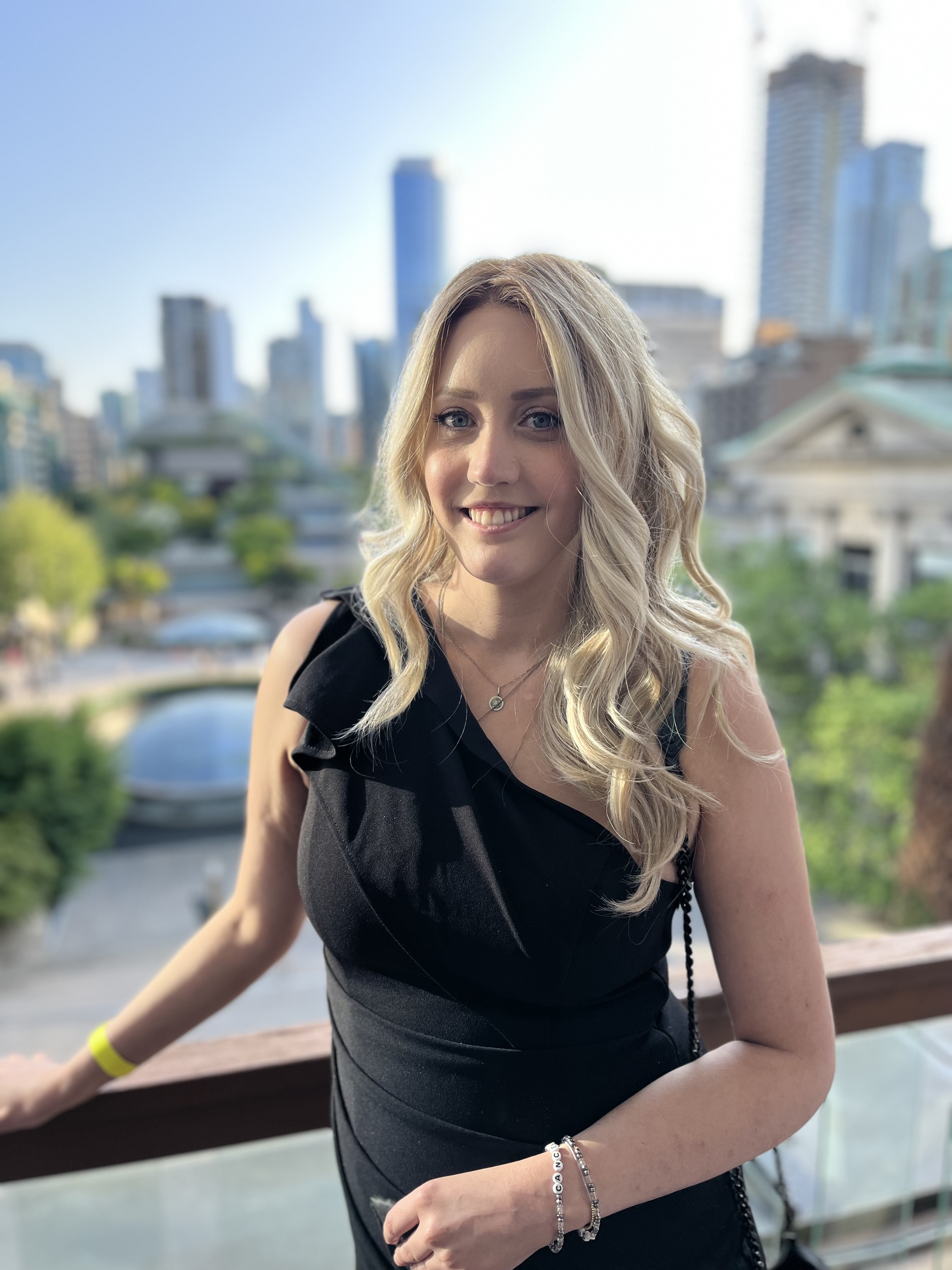 Ashley leaning on a railing with a picturesque view of the city behind hear