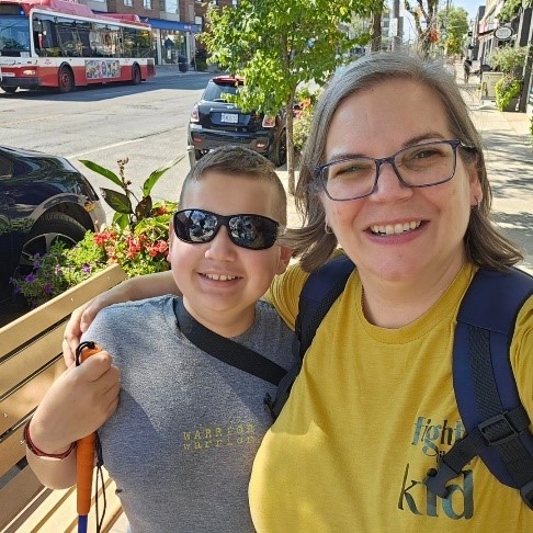 Ollie smiling and hugging his mother Dawn outside beside a bench.