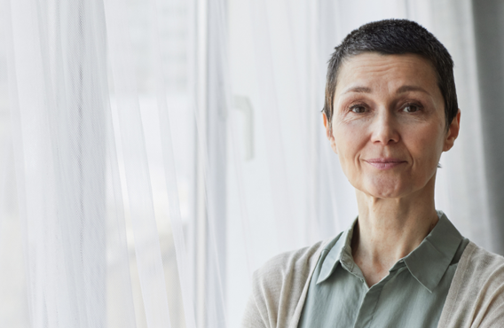 A woman with short gray hair standing by a window with curtains.