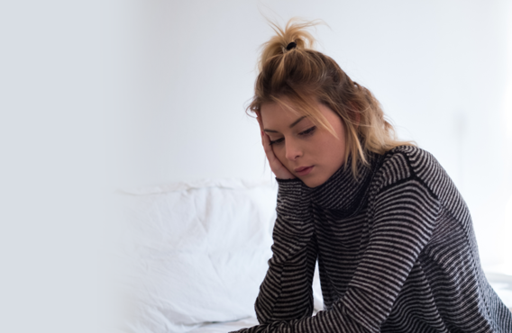 A young woman sitting on her bed looking down at something.