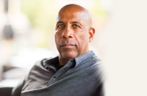 Bald man sitting on a couch in front of a bright background.