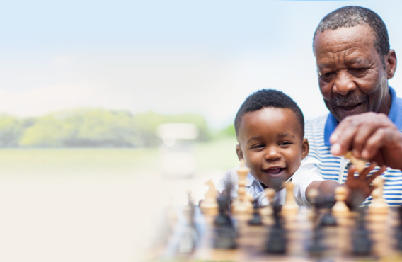 A man and his son playing chess outside in a grassy field.