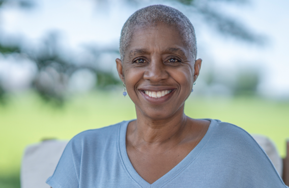 Smiling short grey haired woman outside in front of a field which is blurred.