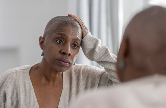 A bald woman looking at herself in a mirror.