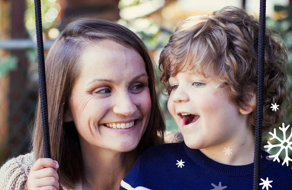 A close up of Beckett and his mother sitting on a swing. Beckett is smiling while looking off and his mother is smiling while looking at Beckett