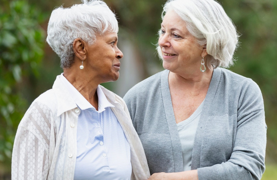 Two women are outside. They are older and looking at each other.
