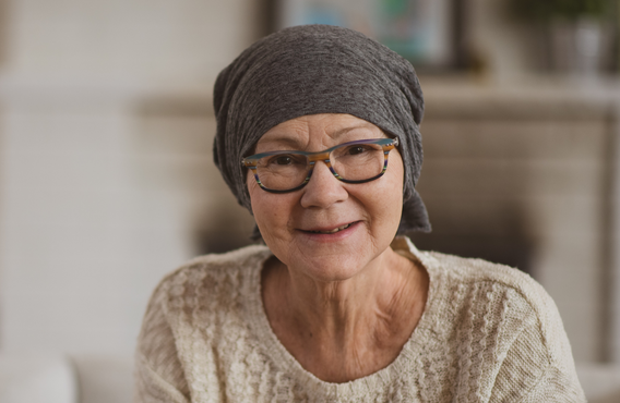 Person wearing a headscarf and glasses seated indoors, facing the camera. Soft, neutral background with warm lighting creates a calm, welcoming setting.