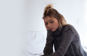 A young woman sitting on her bed looking down at something.