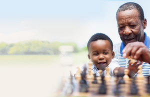 A man and his son playing chess outside in a grassy field.