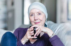 Smiling woman with a cloth wrapped on top of her head sitting on a couch with a coffee mug