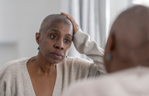 A bald woman looking at herself in a mirror.