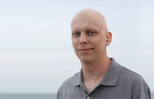 Smiling bald man standing in front of a body of water.