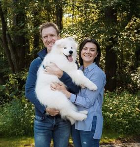 Steve Hopkin and Shannon holding a white dog outside in front of a sunny wooded area.