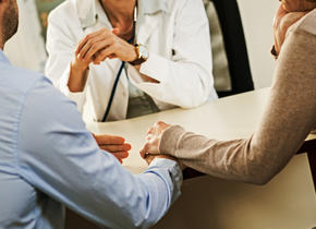 Two people holding hands while talking to a Doctor.