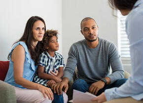 A family of 3 (father, mother, and son) being told some news by a person out of viewpoint.
