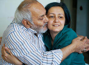 An elderly man giving a woman a hug and a kiss on the cheek.