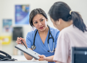 A medical professional points at a chart and explains something to a patient who is facing away from the camera