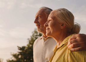 A man and a woman are outside in the golden hour. They are looking off in the distance.