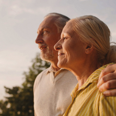 A man and a woman are outside in the golden hour. They are looking off in the distance.