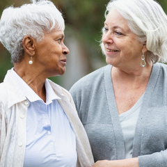 Two women are outside. They are older and looking at each other.