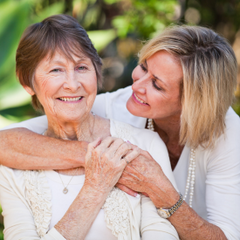 A woman embraces an older woman. They are outside. The older woman is looking at the camera.