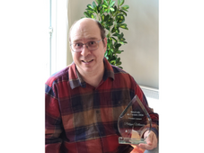 A man in a plaid shirt holds an award.