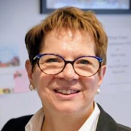 Anna Giulione, a woman with short hair and glasses, smiles at the camera