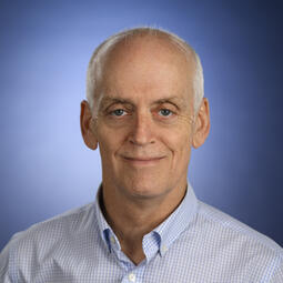 A man in a checkered blue shirt stands in front of a blue background