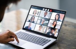 Person viewed from behind participating in a video call, facing a screen with multiple attendees in a grid layout.